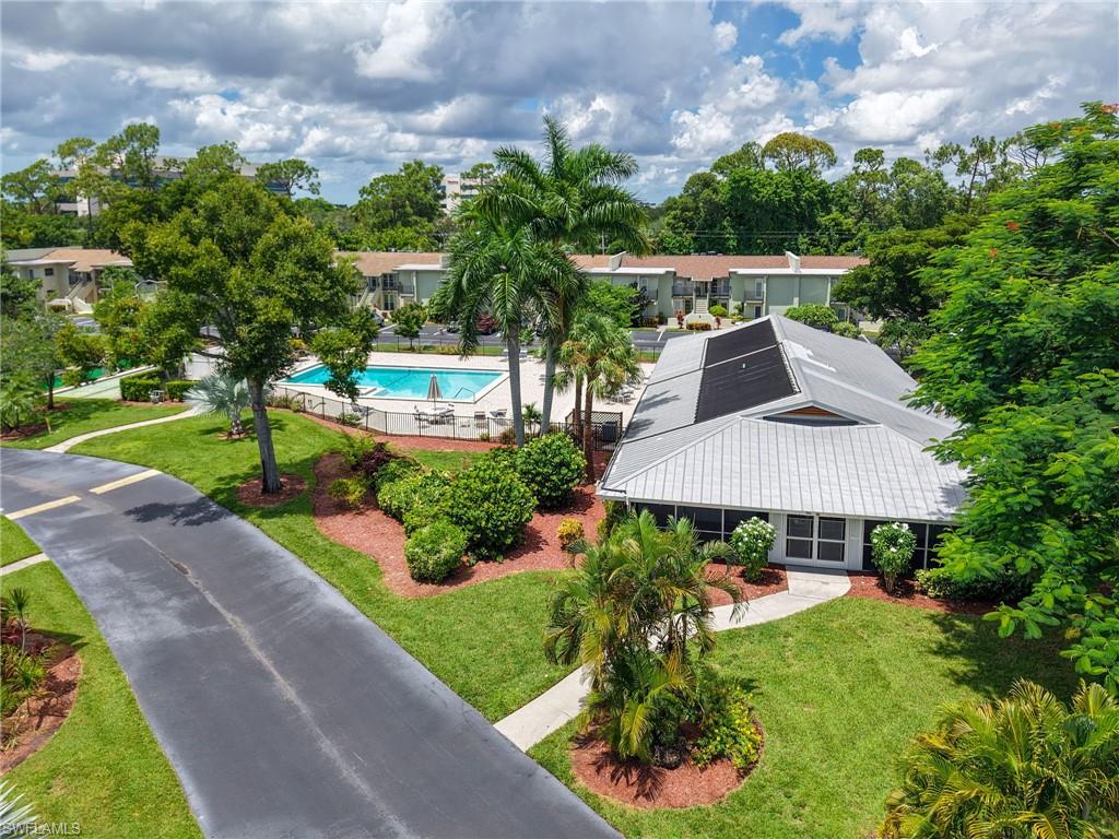 Community building with a metal roof, surrounded by landscaped grounds, a paved pathway, and a swimming pool
