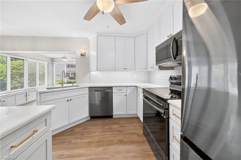White cabinetry with gold-tone hardware, wood-finish flooring, subway tile backsplash, and stainless steel appliances