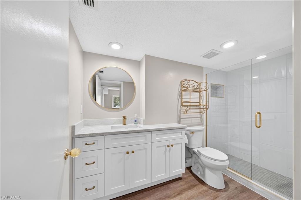 Guest bath with white quartz vanity with a light-toned countertop, gold-finish hardware, and a round wall mirror