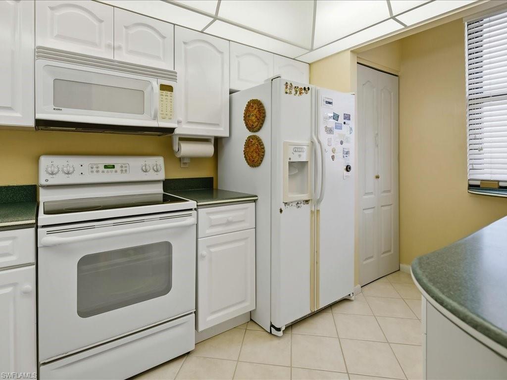 White cabinetry, white appliances, green countertops, and tiled flooring