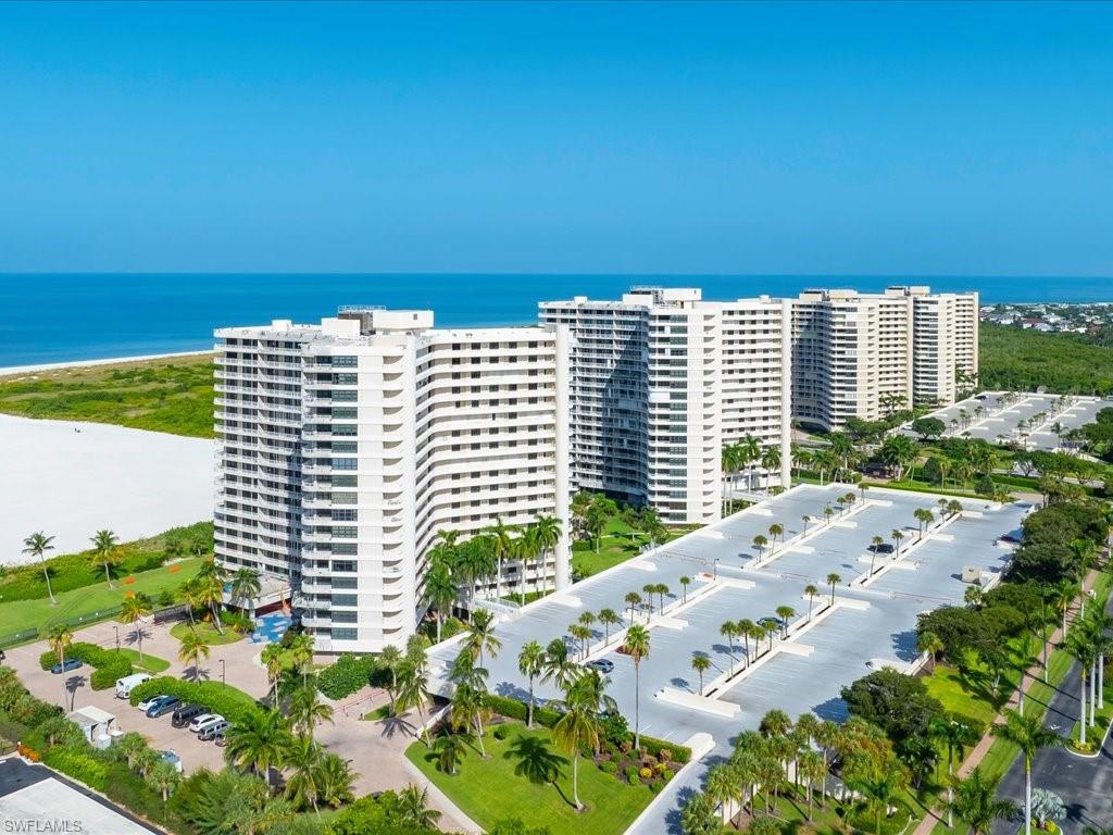 Multi-story residential buildings with multiple balconies, adjacent to a wide sandy beach and ocean