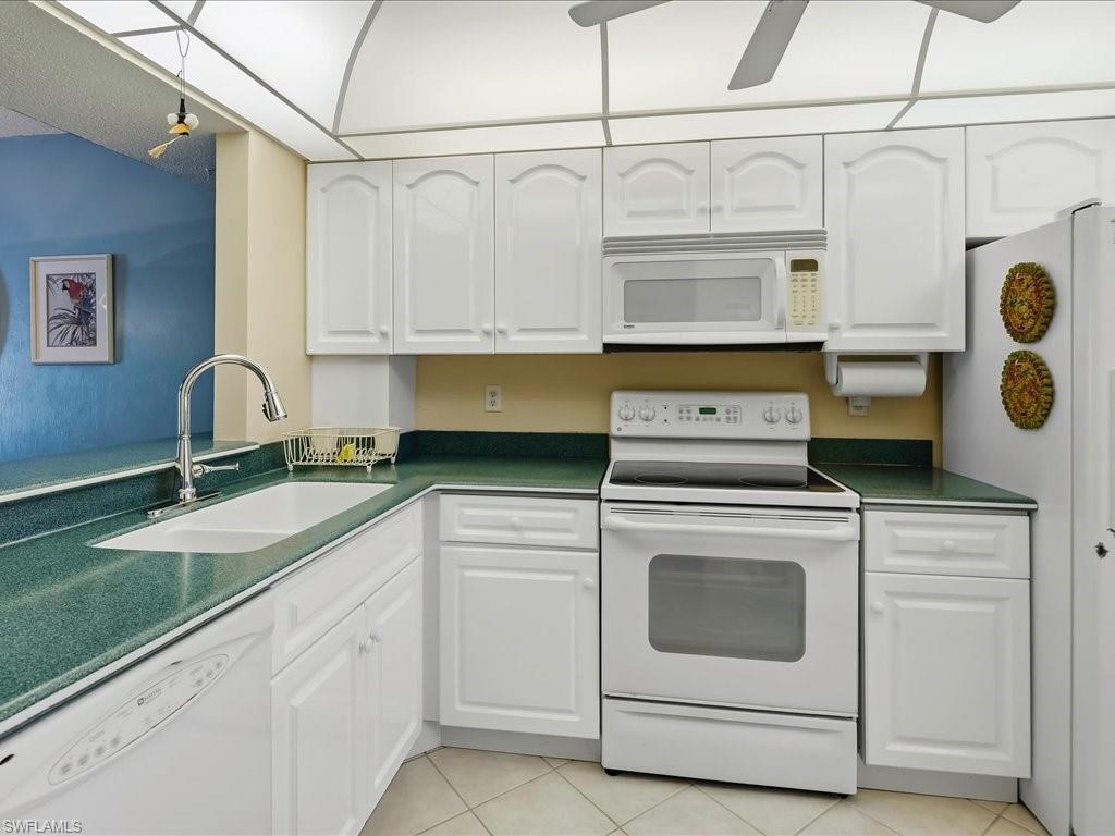 White cabinetry with arched panel doors, green speckled countertops, and integrated white appliances including a range, microwave, and dishwasher