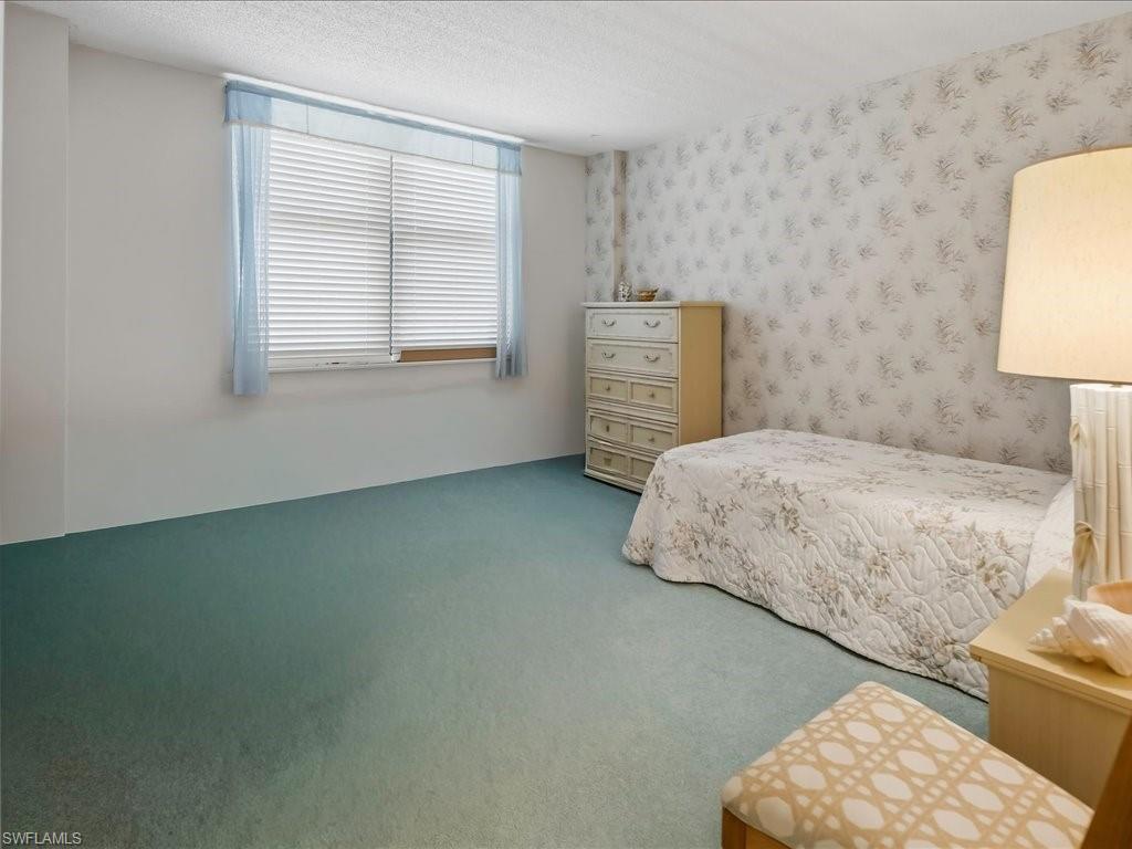 Wall-to-wall carpeting, textured ceiling, a window with horizontal blinds, and a patterned accent wall