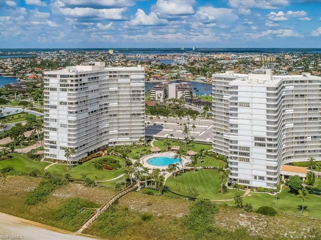 Coastal high-rise residences featuring multiple balconies, a resort-style swimming pool, lush landscaping, and a boardwalk