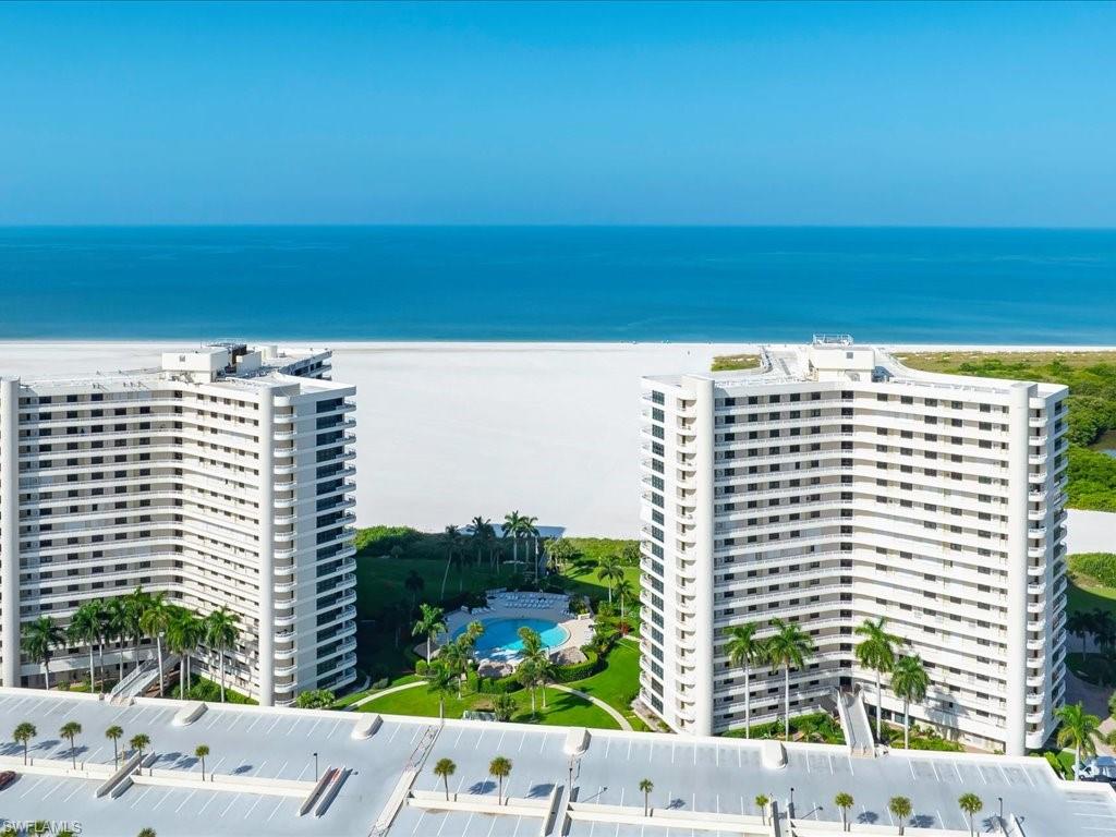 Oceanfront twin high-rise buildings with expansive beachfront access, a large outdoor pool, and abundant palm trees