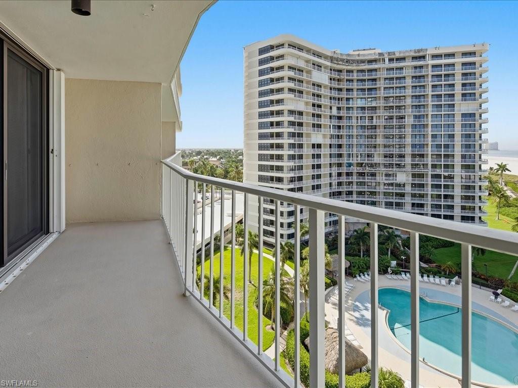 Private balcony featuring a white railing, overlooking a swimming pool, green landscaping, and distant ocean