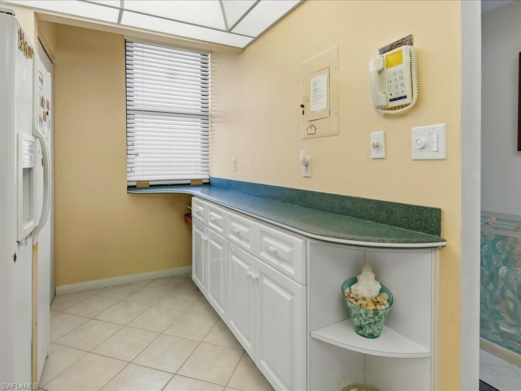 White cabinetry with a green countertop, tiled flooring, and a window with blinds