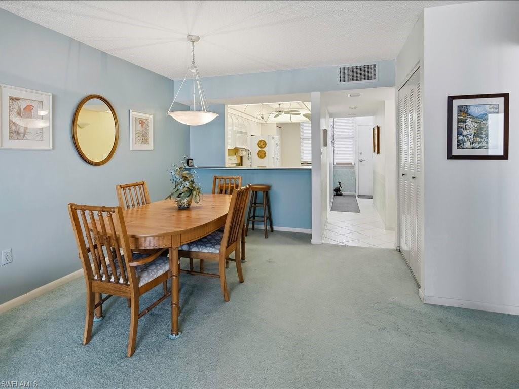 Dining area with a pendant light fixture, carpeted flooring, and a pass-through opening to the kitchen