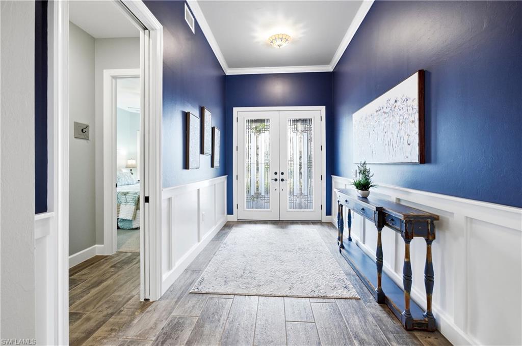 Double entry doors with decorative glass, wood-finish flooring, white wainscoting, and crown molding