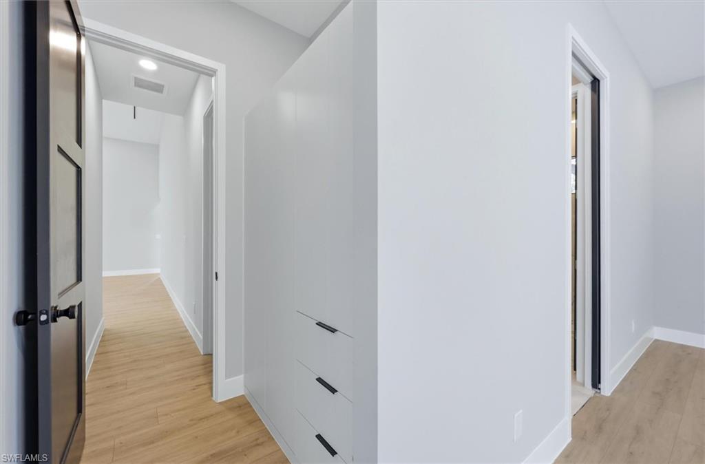 Bright hallway with wood-finish flooring, clean white walls, and built-in storage cabinetry featuring multiple drawers