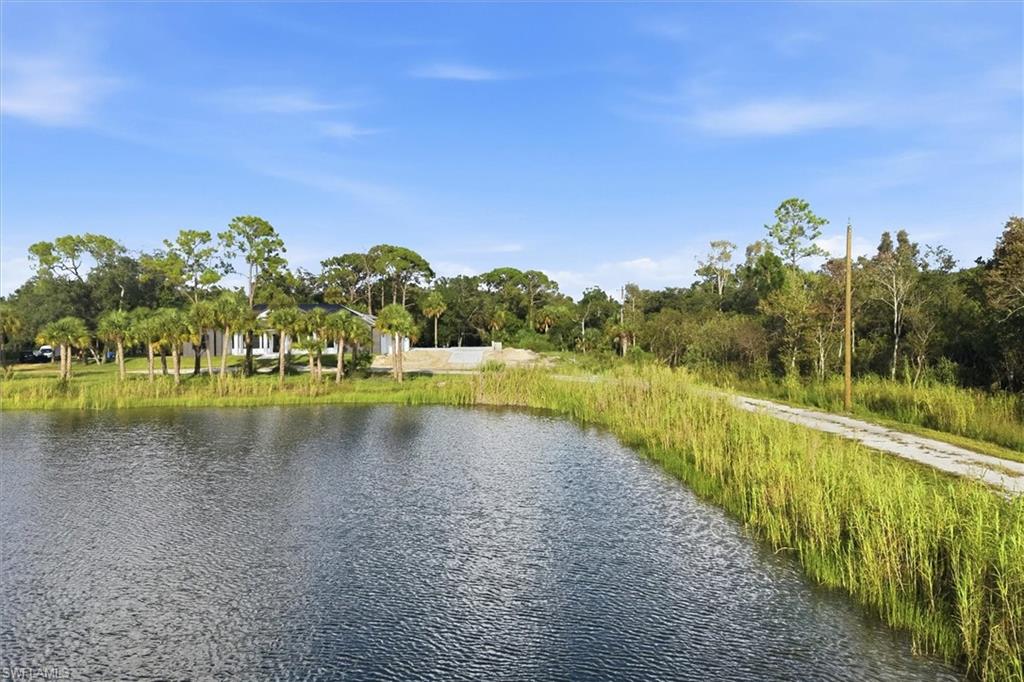 Waterfront property featuring a private pond with mature landscaping, native marsh grasses along the water's edge, a tree-lined perimeter, and a paved pathway providing direct water access