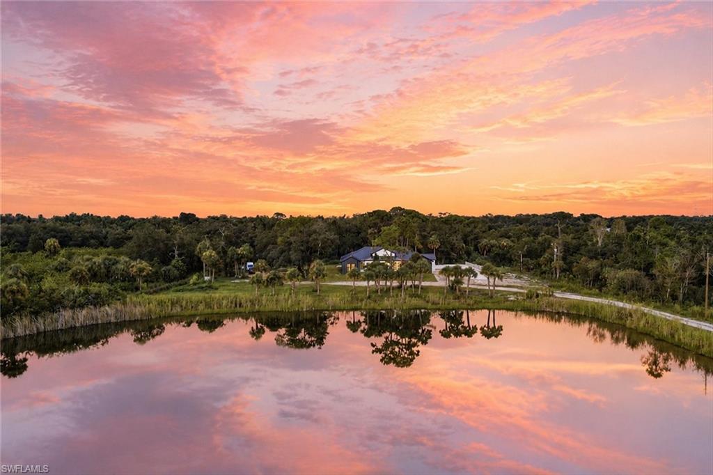 Serene waterfront estate featuring expansive manicured grounds, mature tree-lined landscape, private pond with reflective water frontage, and residential structures set back from the water's edge—offering peaceful pastoral setting with established natural surroundings