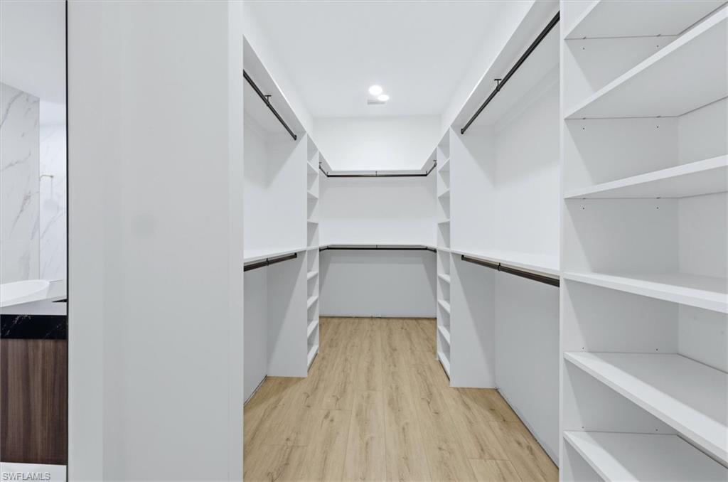 Walk-in closet featuring extensive white built-in shelving, hanging rods, and wood-finish flooring