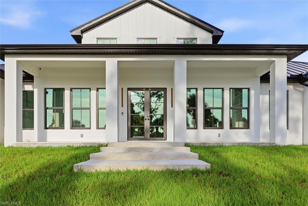 Modern farmhouse exterior with a covered porch, white siding, black-framed windows, and double entry doors