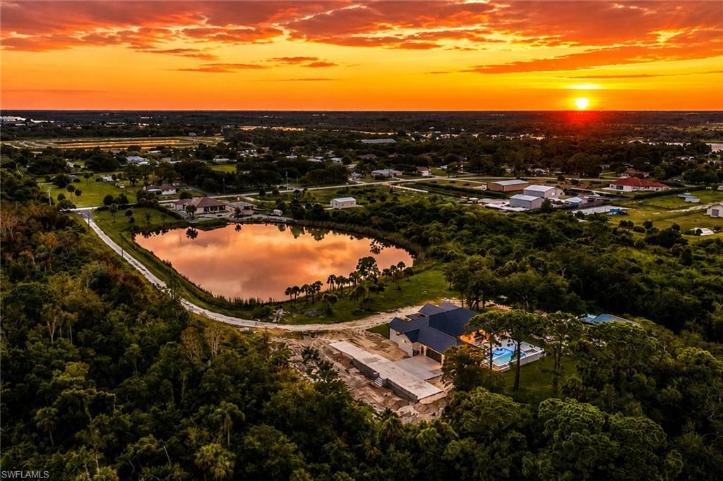 Aerial sunset view showcasing the property's lakefront setting with mature landscaping, manicured grounds, and a modern pool pavilion nestled among established trees