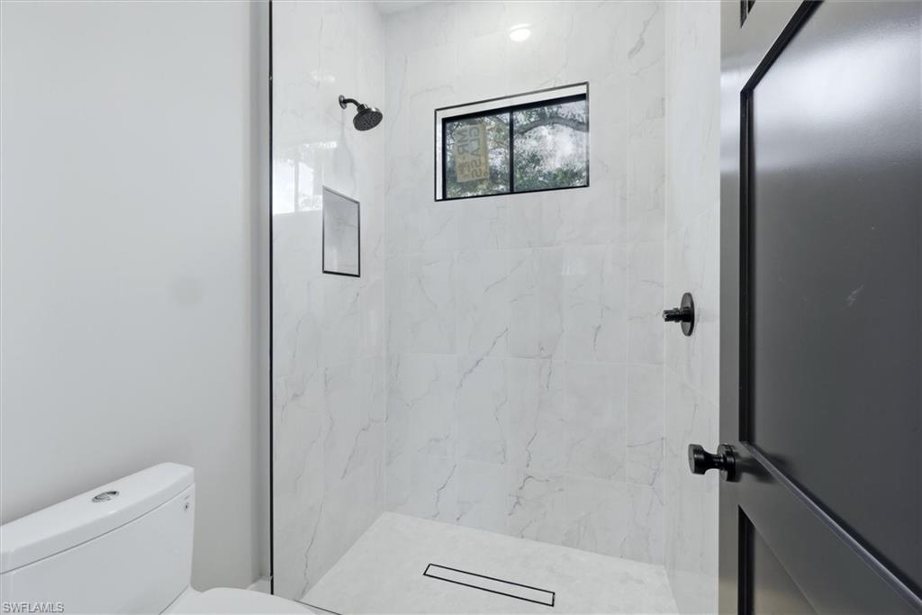 Modern primary bathroom featuring a walk-in shower with marble-look tile walls, a linear drain, and a fixed showerhead with handheld spray