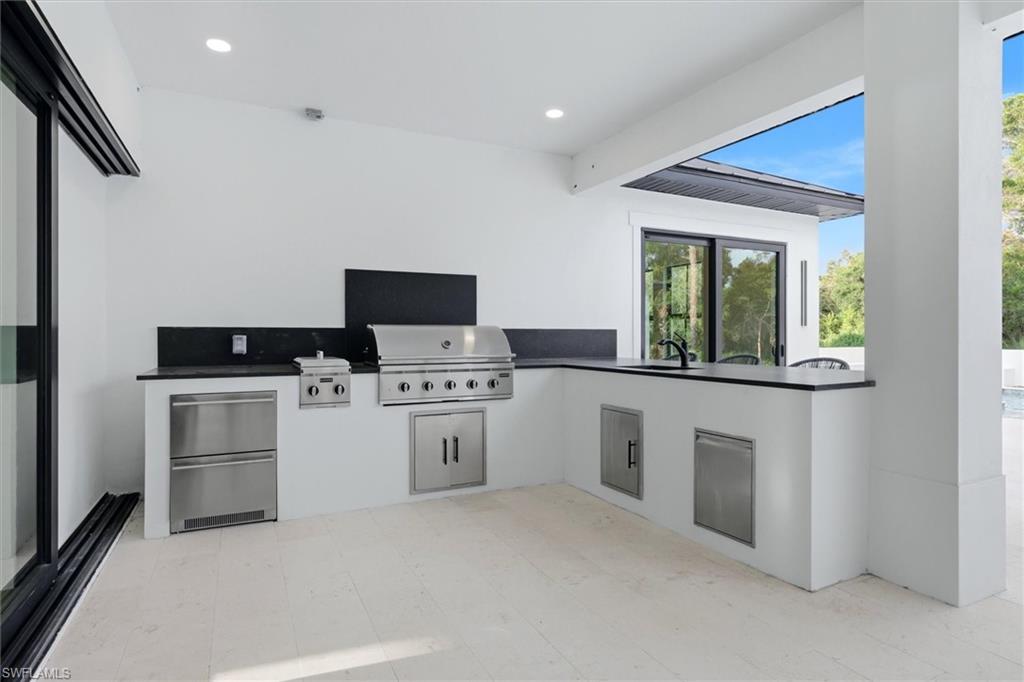 Outdoor kitchen featuring stainless steel grill, integrated appliances, and dark stone countertops