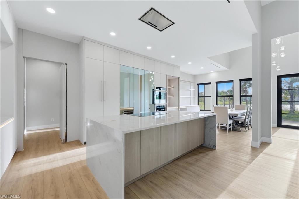 Expansive kitchen island with a light-toned countertop, integrated oven and microwave, recessed lighting, and wood-finish flooring
