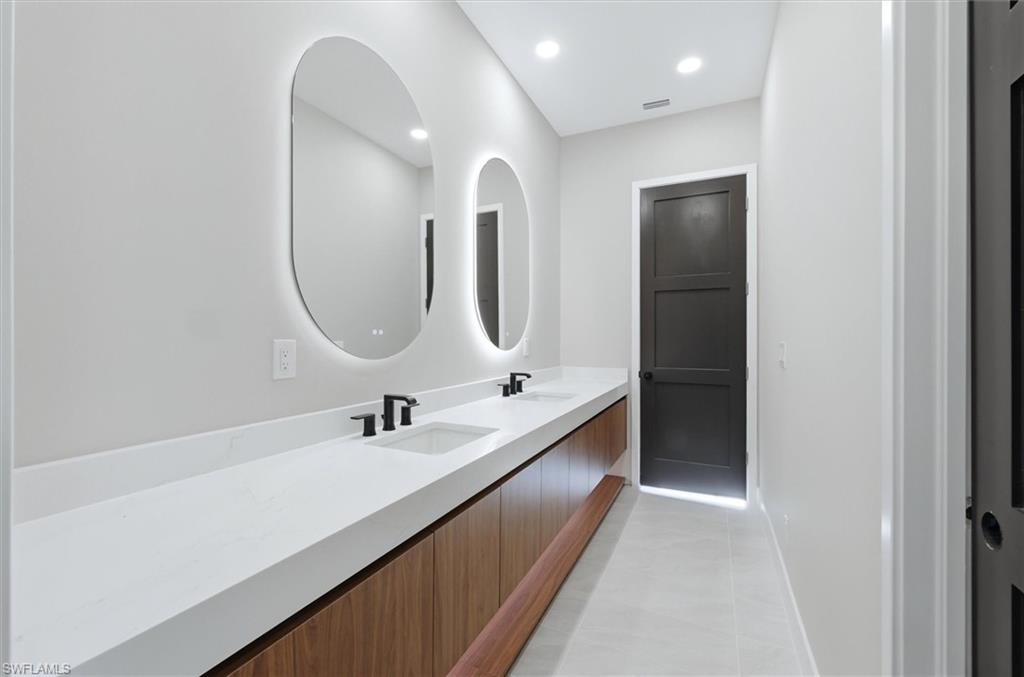 Double vanity with undermount sinks, illuminated oval mirrors, wood-finish cabinetry, and matte black fixtures