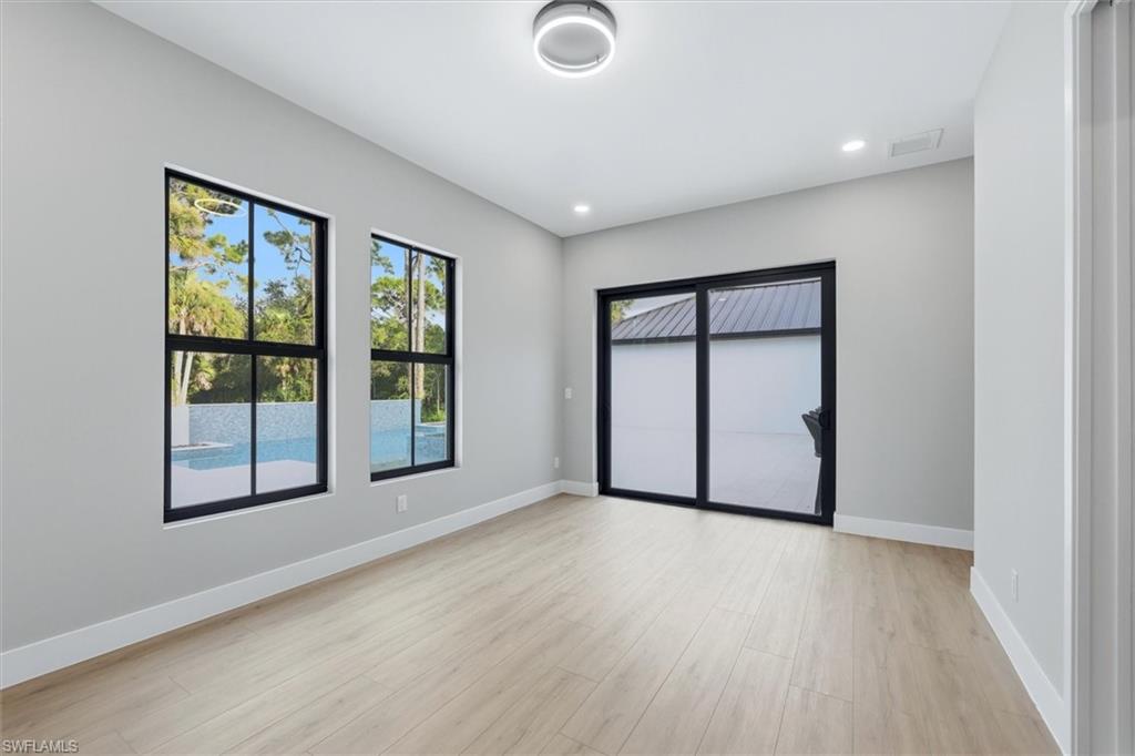 Bright, open room featuring expansive black-framed glass doors and multi-pane windows with water views, light wood-finish flooring, recessed ceiling lighting, and clean white walls ideal for flexible living or workspace use