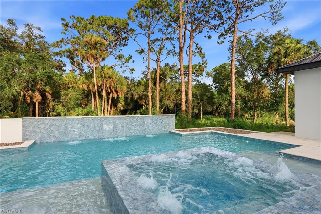 Integrated pool and spa featuring a tiled waterfall wall, multiple water features, and surrounding natural landscaping