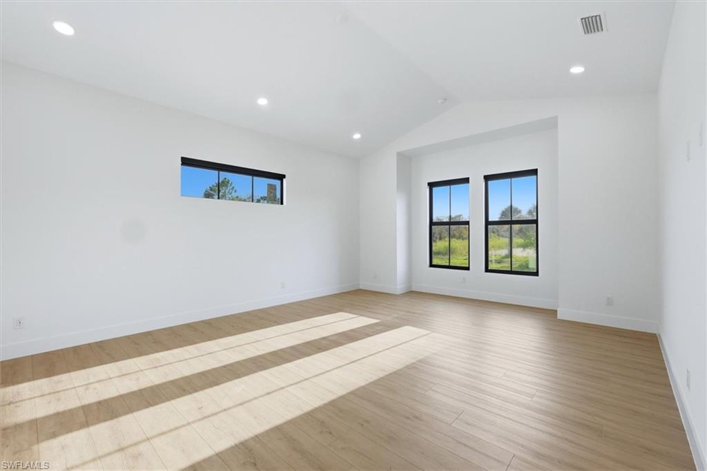 Vaulted ceiling, recessed lighting, light wood-finish flooring, multiple windows, and white walls