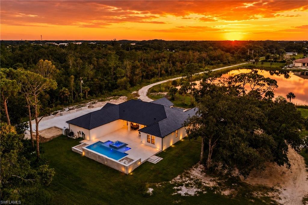 Modern residence featuring a striking black hip roof and light-finished exterior, positioned on expansive manicured grounds with mature landscaping