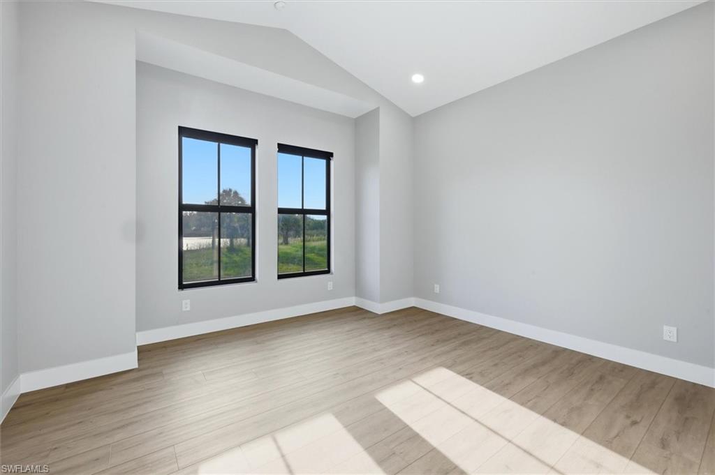 Bright corner bedroom featuring dual black-framed windows with expansive natural light, wood-finish flooring, and clean white walls with recessed ceiling lighting