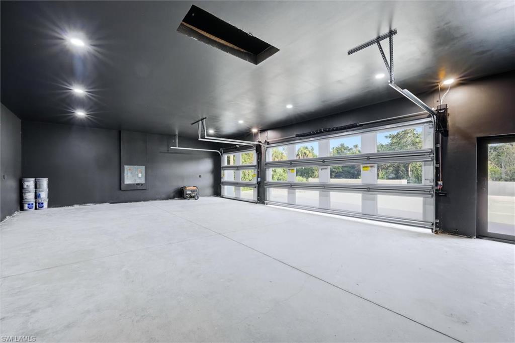 Spacious garage featuring polished concrete flooring, modern recessed and pendant lighting, glass overhead door with natural light, and black finished walls with contemporary hardware and storage infrastructure