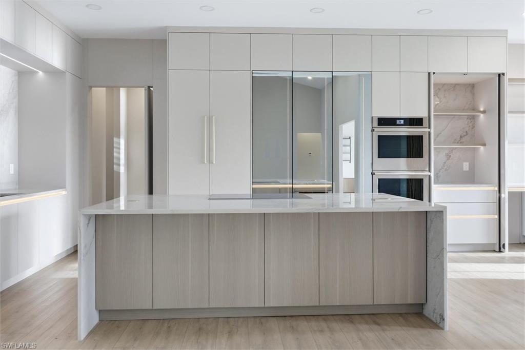 Contemporary kitchen featuring a waterfall-edge island with wood-finish cabinetry, white quartz countertops, and integrated seating
