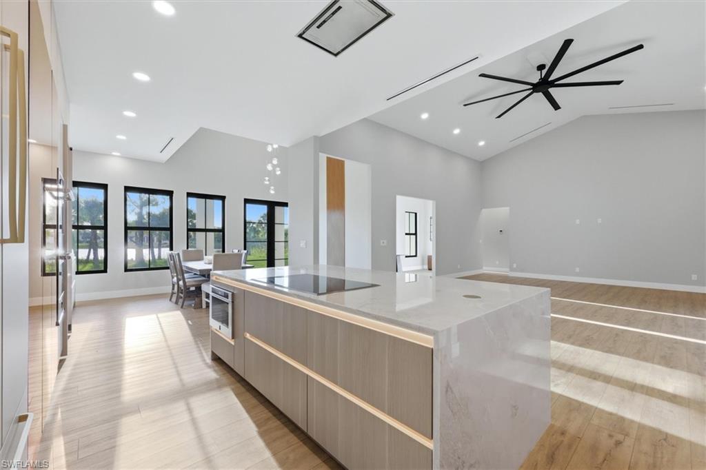 Modern open-concept kitchen and living area featuring a large waterfall-edge island with wood-finish cabinetry, white quartz countertops, and stainless steel appliances