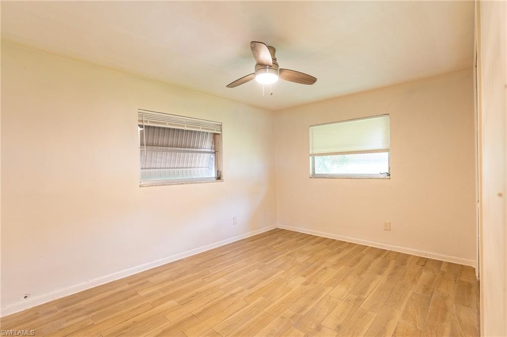 Bright, light-filled bedroom showcasing warm wood-finish flooring, ceiling fan with integrated lighting, and dual windows providing natural illumination