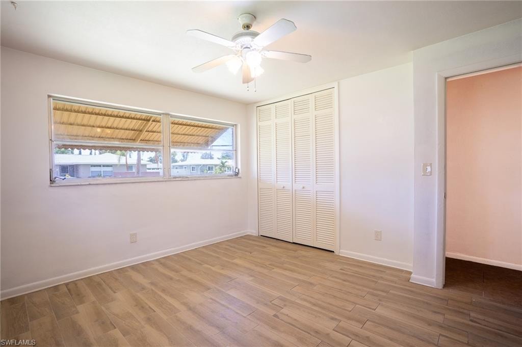 Wood-finish flooring, white walls, louvered bi-fold closet doors, and a ceiling fan with integrated lighting