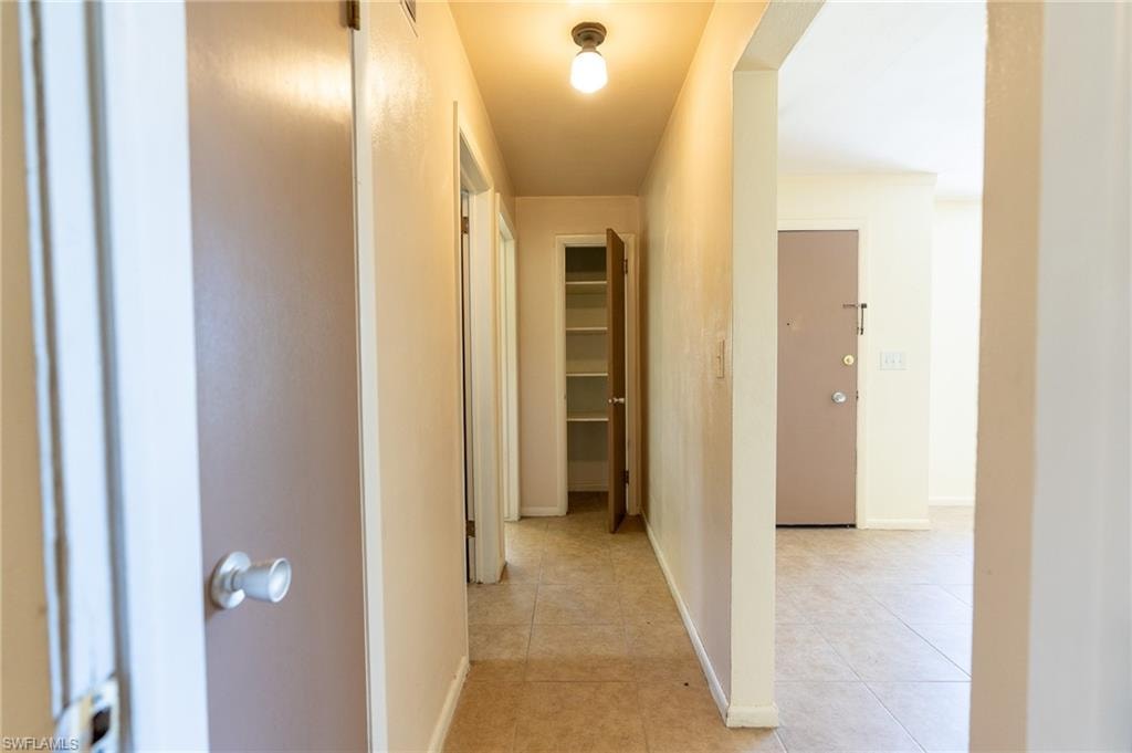 Hallway with tile flooring, featuring an overhead light fixture, light beige wall paint, and a built-in shelving unit