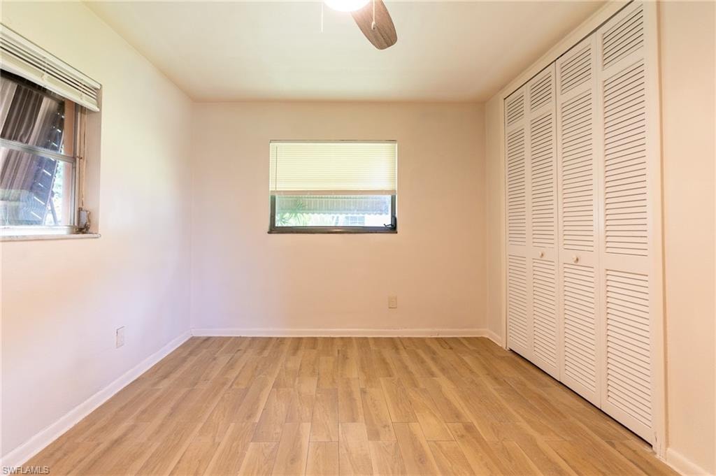 Wood-finish flooring, white walls, two windows, louvered bi-fold closet doors, and an attached ceiling fan