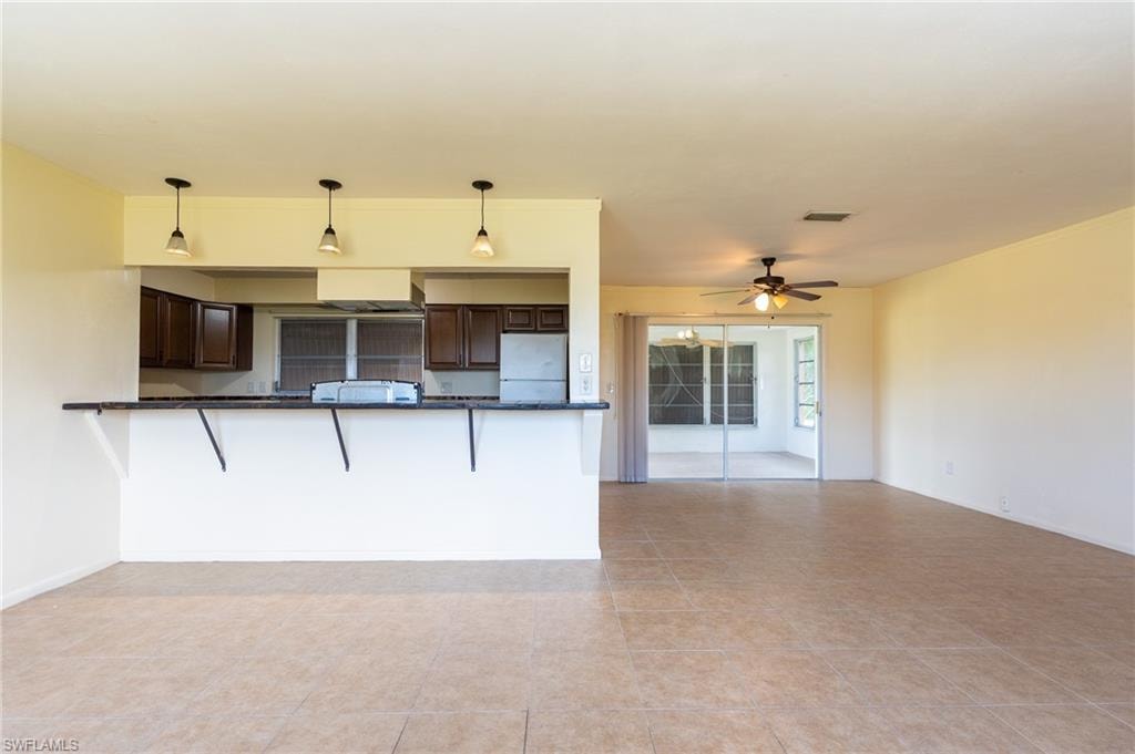 Open-concept living and kitchen area featuring tile flooring throughout, dark wood cabinetry with stainless steel appliances, pendant lighting above the kitchen counter, and sliding glass doors providing natural light