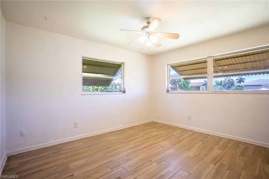 Bright, light-filled bedroom showcasing wood-finish flooring, ceiling fan with integrated lighting, and dual windows with exterior shades allowing natural light and privacy control