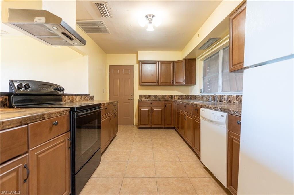 Kitchen featuring wood-finish cabinetry, solid surface countertops, tile flooring, and integrated appliances