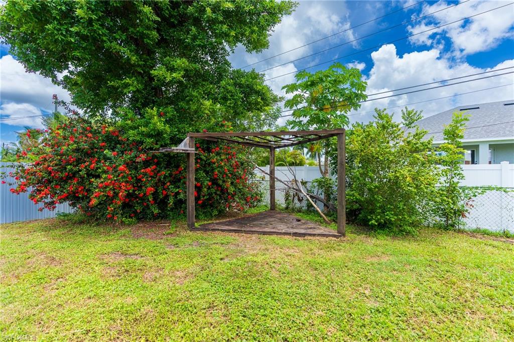 Expansive grassy area featuring a wooden pergola and mature trees with flowering shrubs