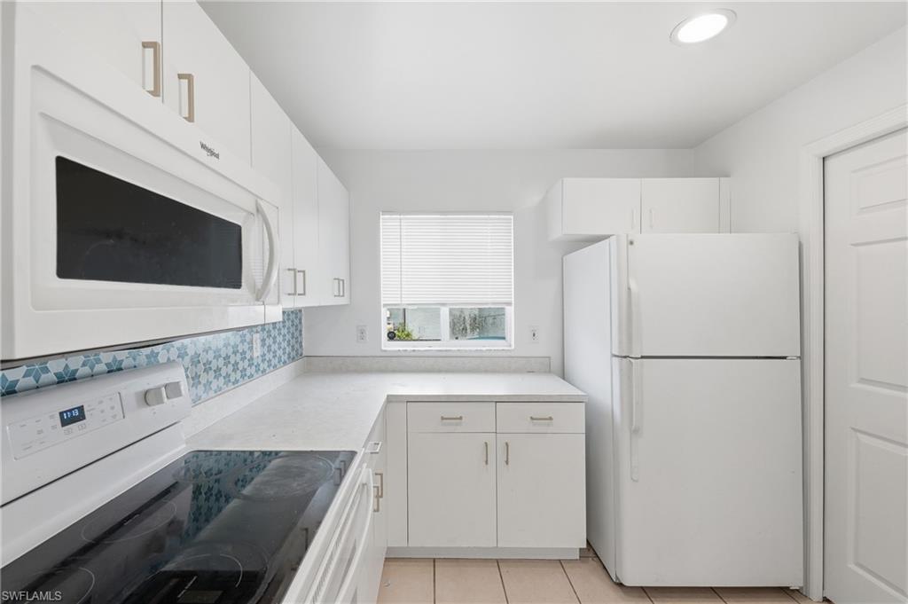 White cabinetry, patterned tile backsplash, solid surface countertops, built-in microwave, and tile flooring