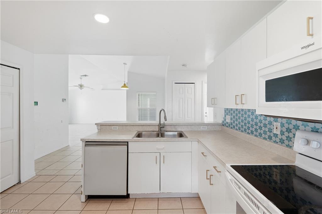 Kitchen featuring white cabinetry, a double basin stainless steel sink, a tile backsplash with a star pattern, a built-in microwave, and a dishwasher