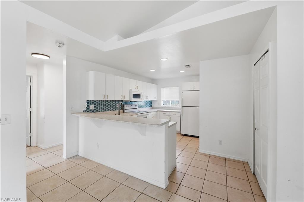 Kitchen featuring white cabinetry, tile backsplash, stainless steel appliances, and a breakfast bar