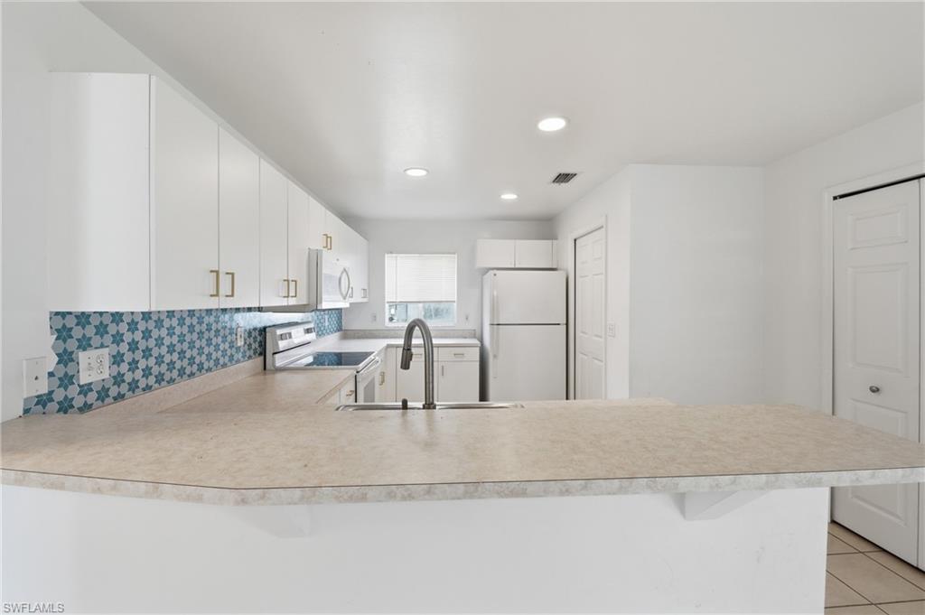 Kitchen featuring white cabinetry, patterned tile backsplash, light-toned countertops, and recessed lighting