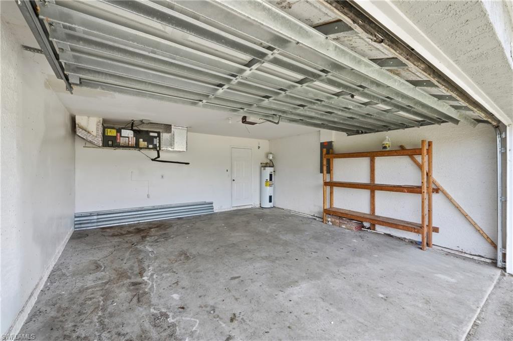 Concrete flooring, white painted walls, water heater, wood shelving, and garage door mechanism