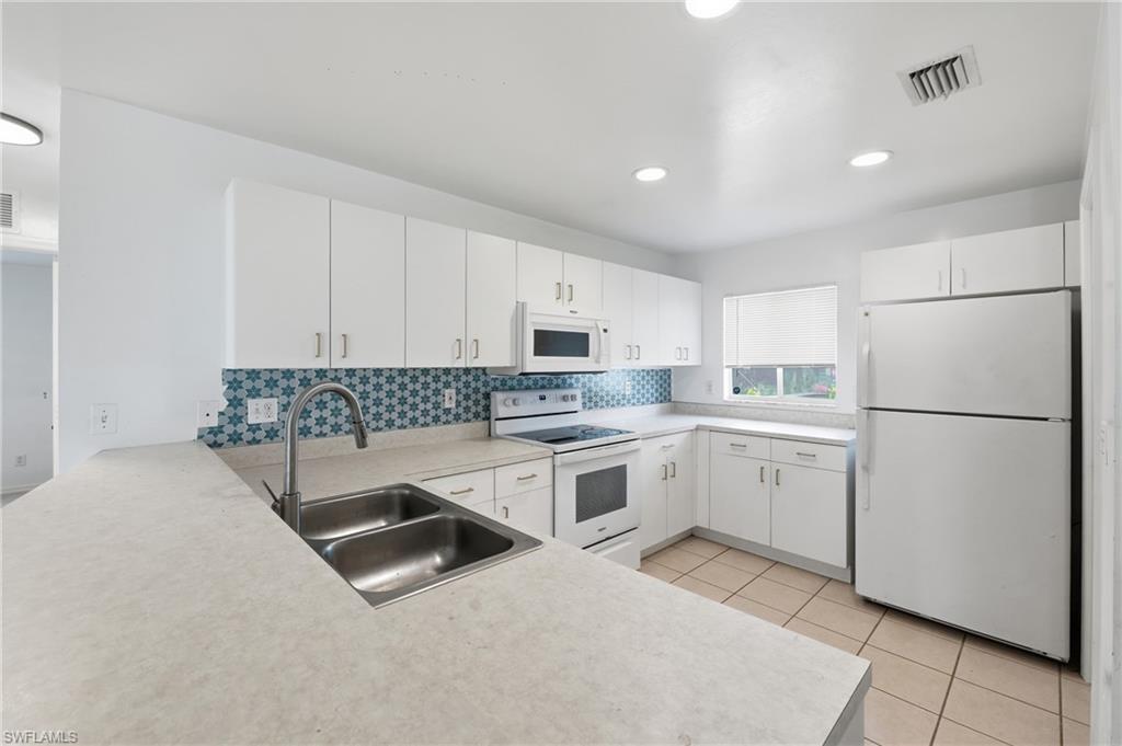 White cabinetry, patterned tile backsplash, stainless steel double basin sink, recessed lighting, and tile flooring