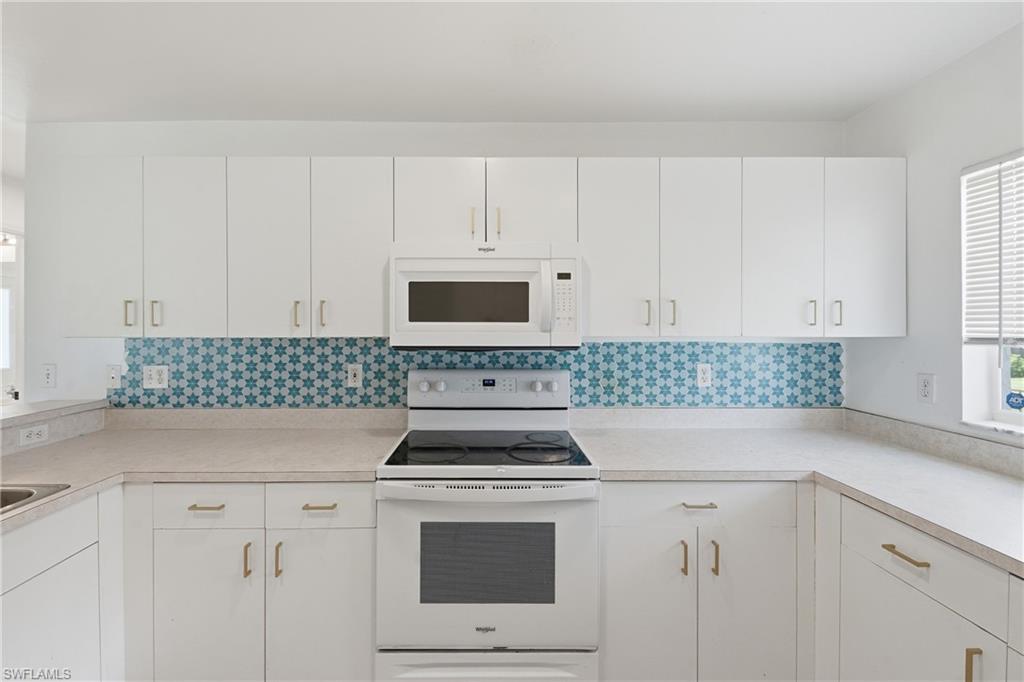 White cabinetry with gold-tone hardware, geometric pattern tile backsplash, white microwave, white range, and light-toned countertops