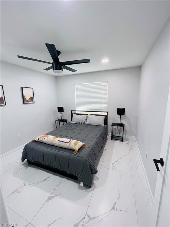 Modern kitchen with white cabinetry and stainless steel appliances, featuring a large center island with a light-toned countertop, white marbled-look tile flooring, and recessed ceiling lighting