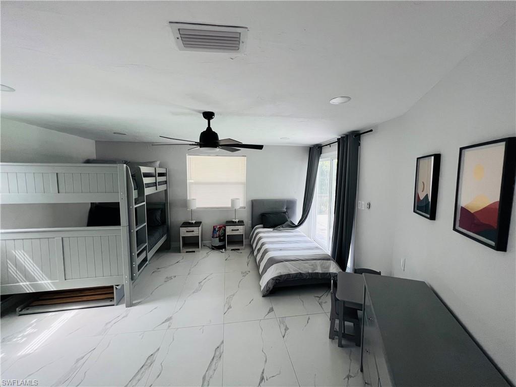 White tile flooring with subtle veining, dark wood-finish vanity with a white countertop, wall-mounted mirror, and a tub-shower combination with glass enclosure