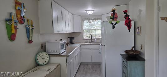 Efficient kitchen space featuring white cabinetry, light countertops, stainless steel sink with a gooseneck faucet, window with blinds, and wood-finish flooring