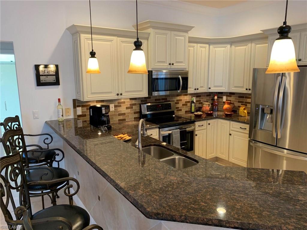 Kitchen featuring appliances with stainless steel finishes, dark stone counters, kitchen peninsula, decorative light fixtures, and a breakfast bar area